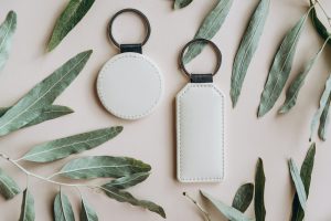 Keychain mockup among olive leaves to display design. Blank white sublimation key chain photo.